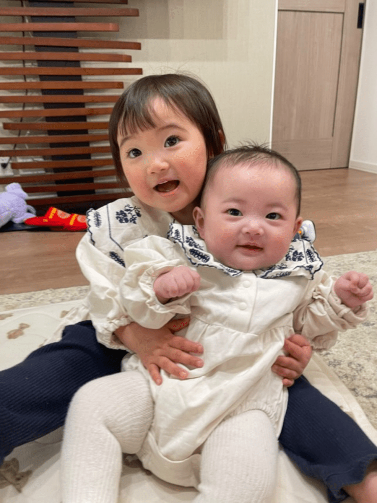 お姉ちゃんの足の間にお座りして微笑む妹ちゃん（@__sr.naさんより提供）