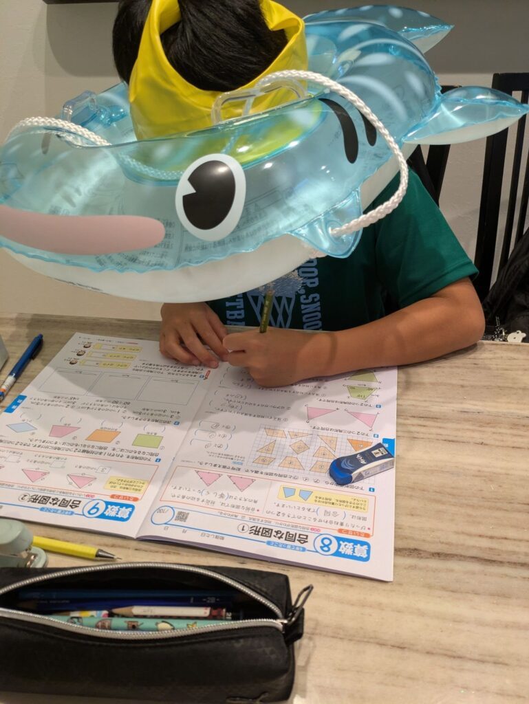 ジンベエザメの浮き輪を被って宿題する息子さん（＠yumama925さんより提供）